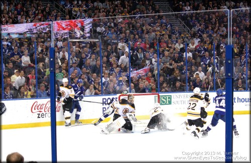 A spray of snow as players rush to the net. Bruins goalie, Rask, defends.